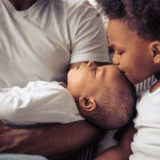 Beautiful young afro american family spending time together. little baby is sleeping in dad's arms while her sister is kissing her