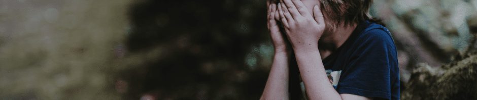 Explosive Child - Young child standing outside with hands firmly covering their face. Gray tone to photograph