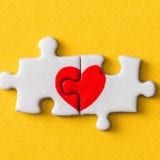 at-risk emotions, connected heart jigsaw puzzle pieces over yellow background