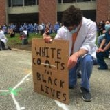 Healthcare worker kneeling with a sign that says "White coats for Black Lives Matter"