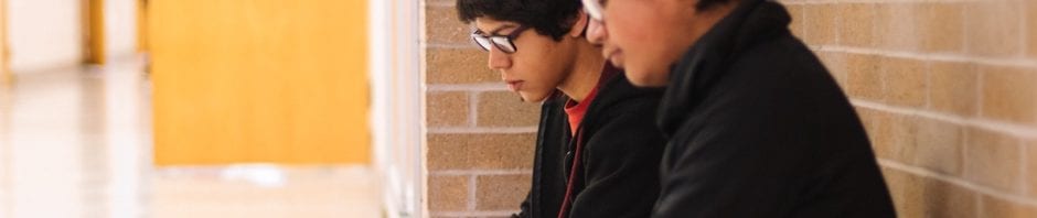 Two Latinx boys sitting in a school hallway together