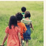 Young kids walking in a line into a green field