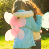 Behind shot of two children wearing fairy wings hugging each other