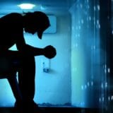 Young man sits on ledge in dark room with elbows on knees, looking down