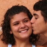 Young teen girl smiling while young teen boy kisses her cheek