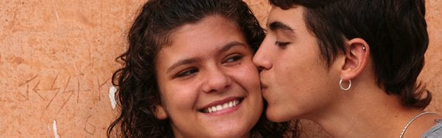 Young teen girl smiling while young teen boy kisses her cheek