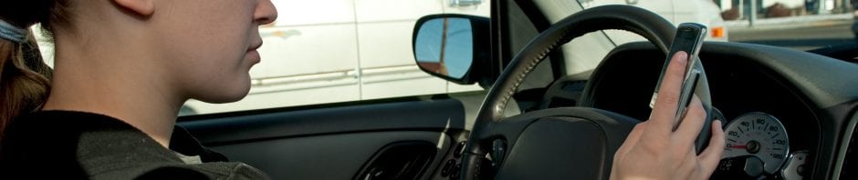 Girl texting with cell phone while driving, hand on steering wheel