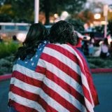 Two individuals walking with backs to camera, draped in American flag