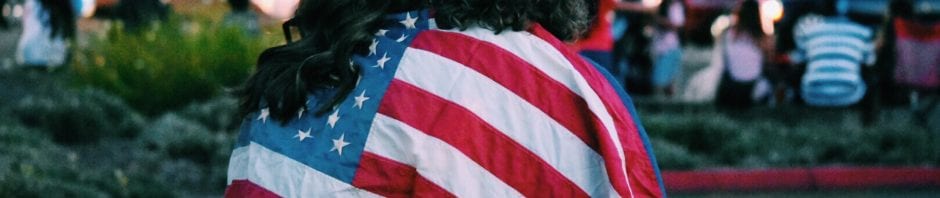 Two individuals walking with backs to camera, draped in American flag