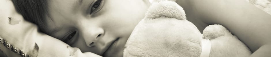 Sepia tone photo of young child cuddling their teddy in bed - measles, flu