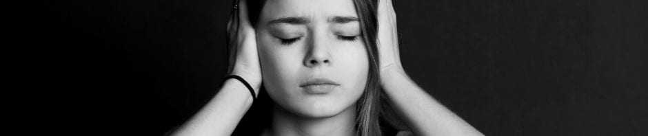 Black and white image of young teen girl closing her eyes and covering her ears with her hands