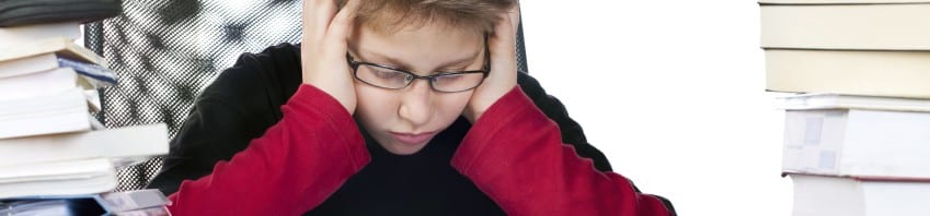 attention deficit - boy sitting at desk piled with books