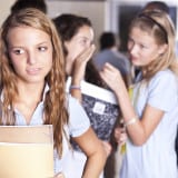 Middle School - Young teen standing at lockers with other teens in the background