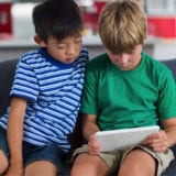 Media literacy - Social Media Mental Health - Two grade school-age siblings using a digital tablet on the couch