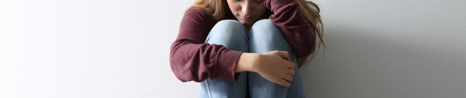 Teen sitting against wall with knees to chest and holding head in hand